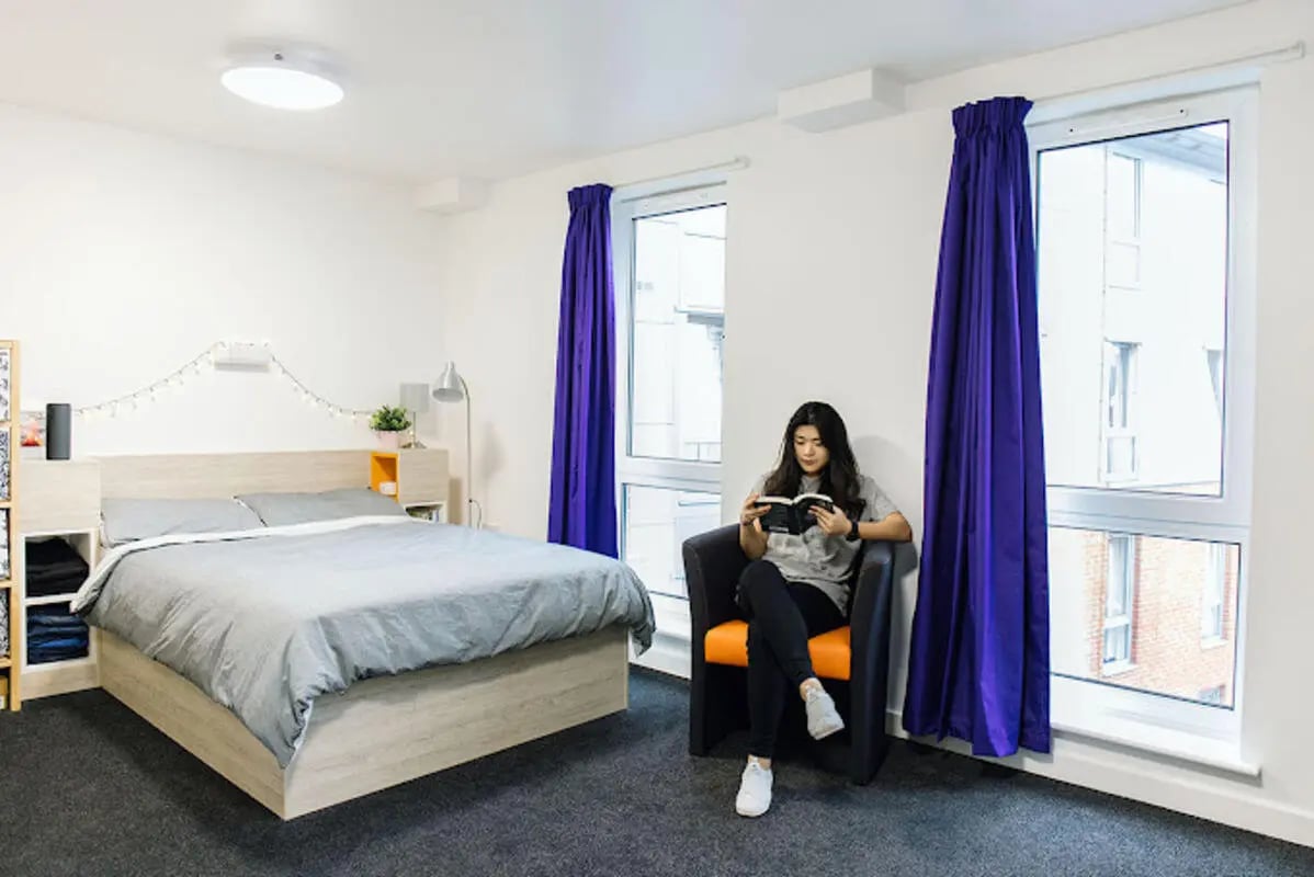 Bed with grey bedding and armchair study area bedroom at Queen's Park House in Coventry Student Accommodation
