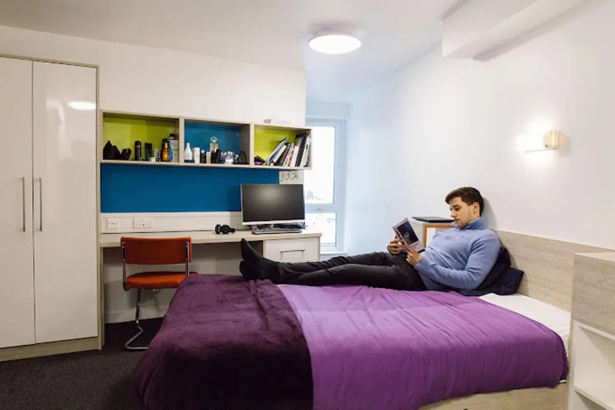 Man reading on bed with desk and wardrobe Bedroom at Queen's Park House in Coventry Student Accommodation