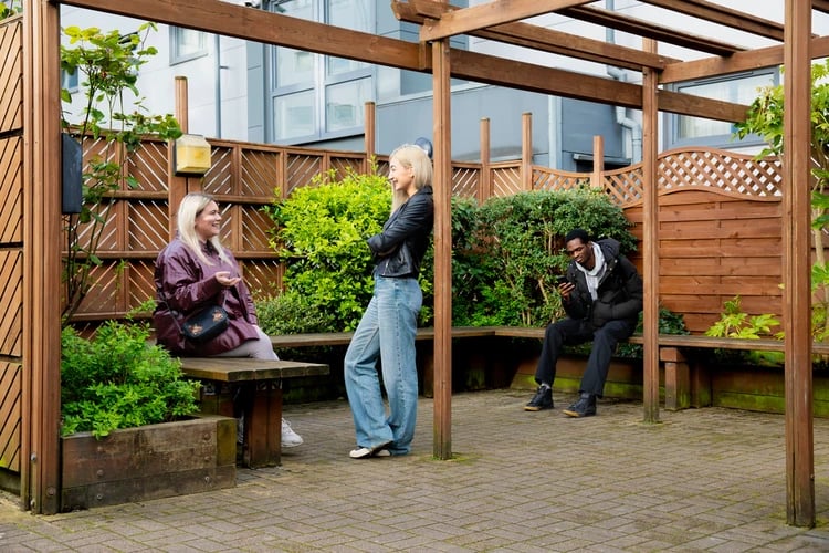 People relaxing on wooden benches in courtyard exterior at Liberty Park in Leicester Student Accommodation