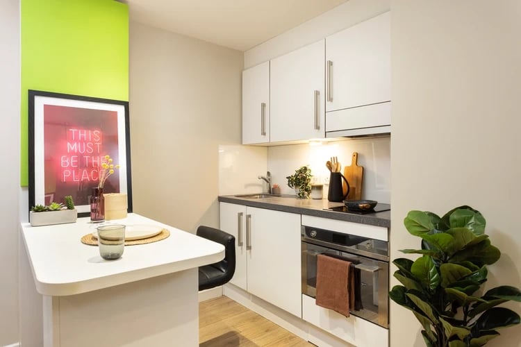 White cabinets stove sink table with art kitchen at Drapery Place in London Student Accommodation