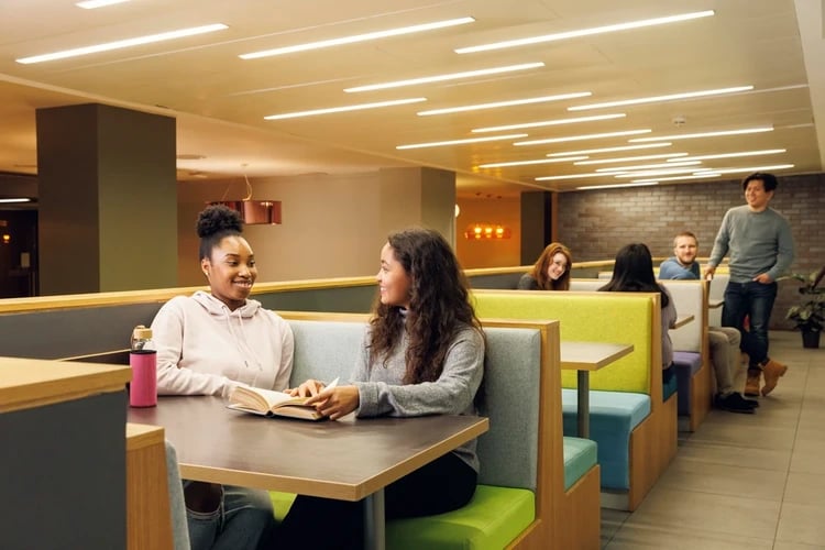 Students chatting at booths with book and water bottle common area at Drapery Place in London Student Accommodation