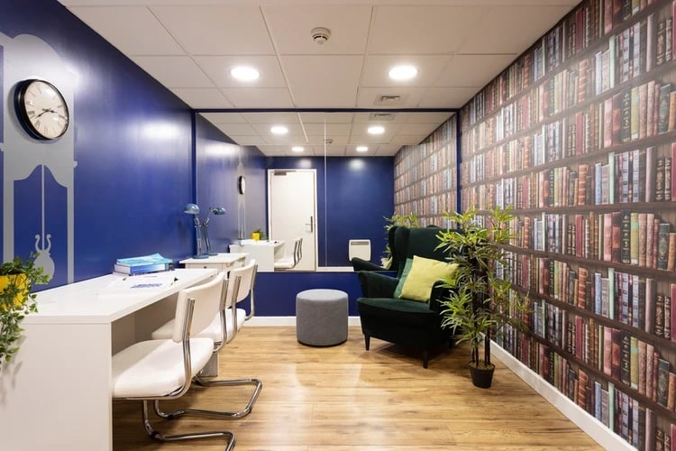Desks chairs armchair and bookshelf wallpaper common area at Drapery Place in London Student Accommodation
