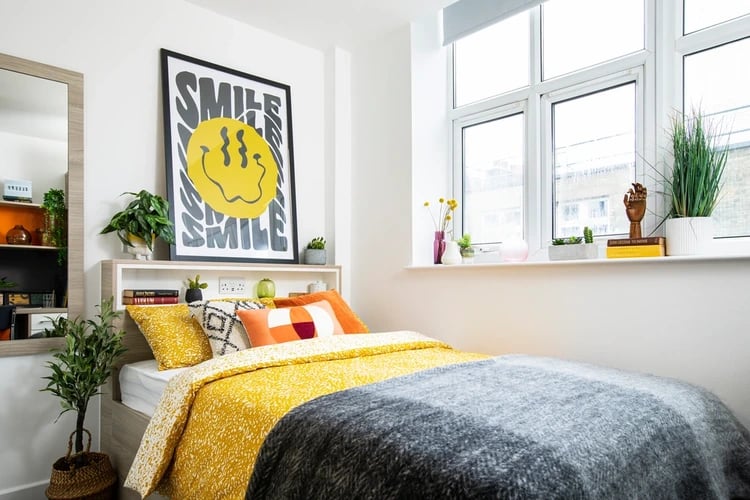 Bed with yellow bedding and smile poster bedroom at Arbour House in London Student Accommodation