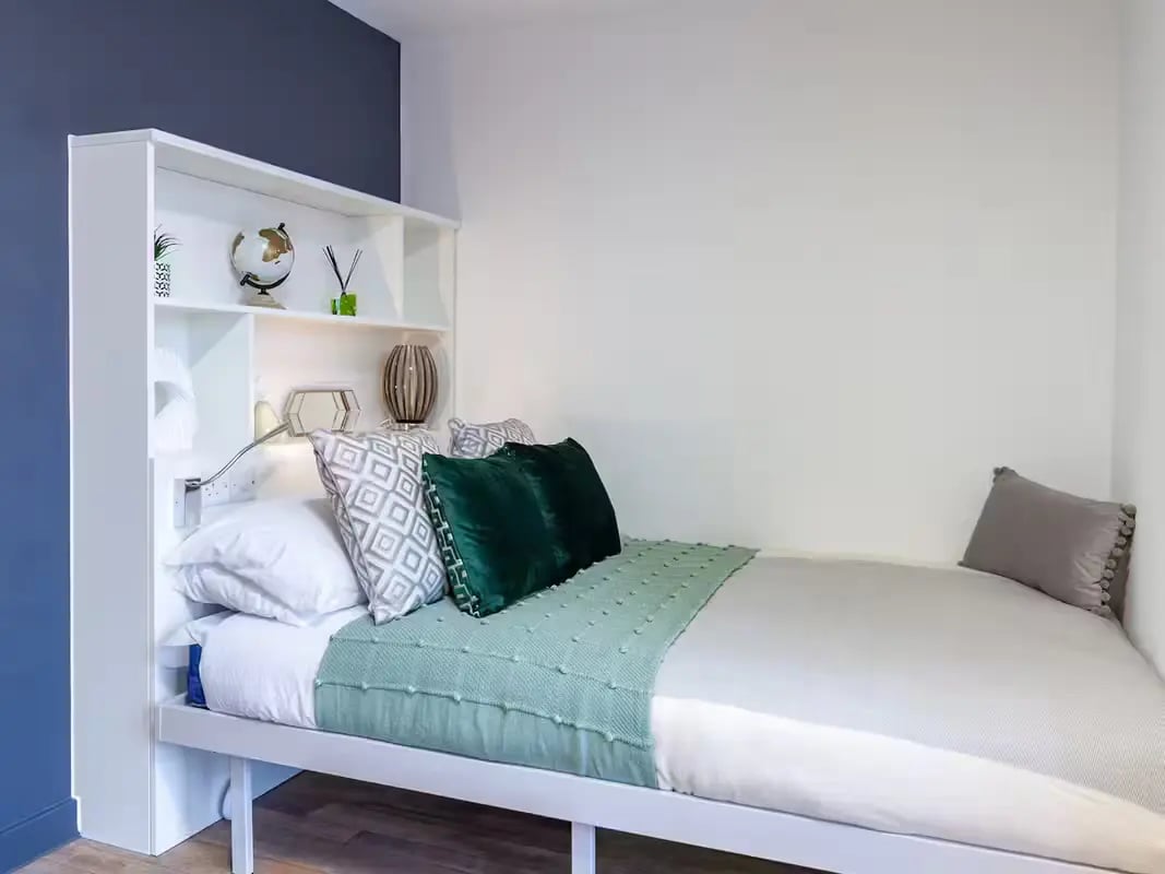 Bed with shelves pillows and green throw bedroom at Plymouth Cross House in Plymouth Student Accommodation