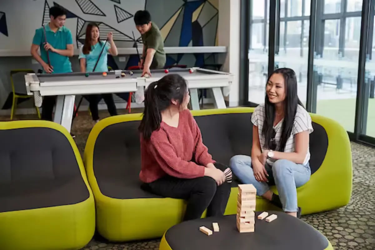 Billiard table and lounge seating with people playing living room at Scape Berkeley 2 in Melbourne Student Accommodation