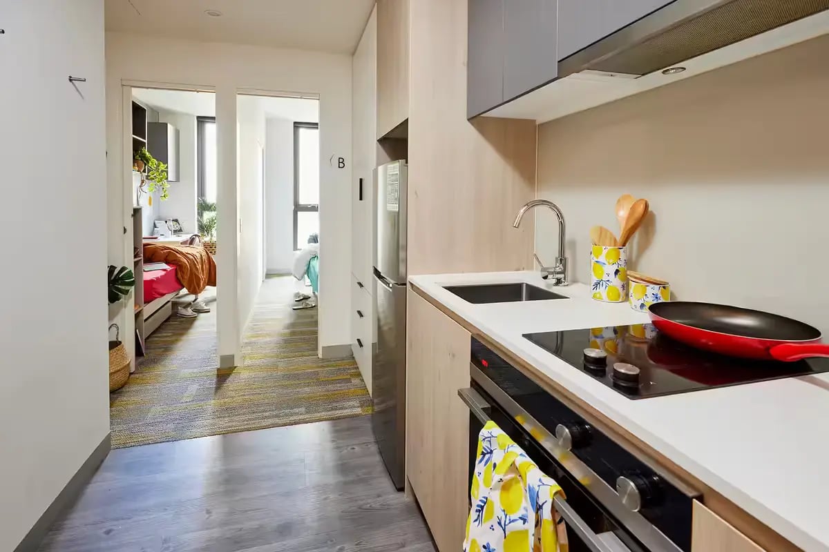 Kitchen with sink stovetop red pan student bedrooms beyond kitchen at Scape Berkeley 2 in Melbourne Student Accommodation