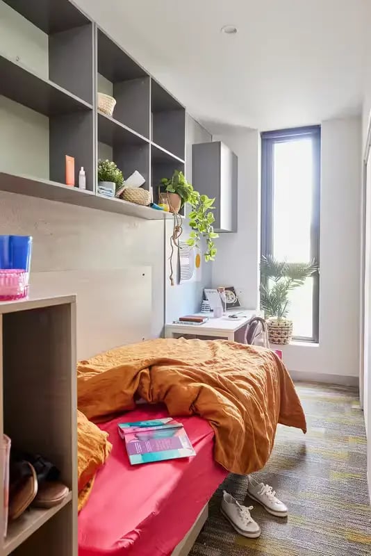 Bed, desk, shelves, window student bedroom at Scape Berkeley 2 in Melbourne Student Accommodation