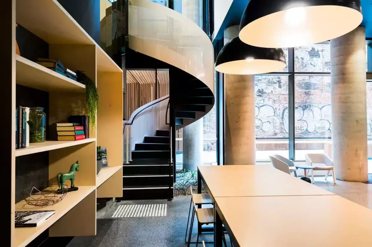 Bookshelf spiral staircase long table and chairs communal area at Scape La Trobe in Melbourne Student Accommodation