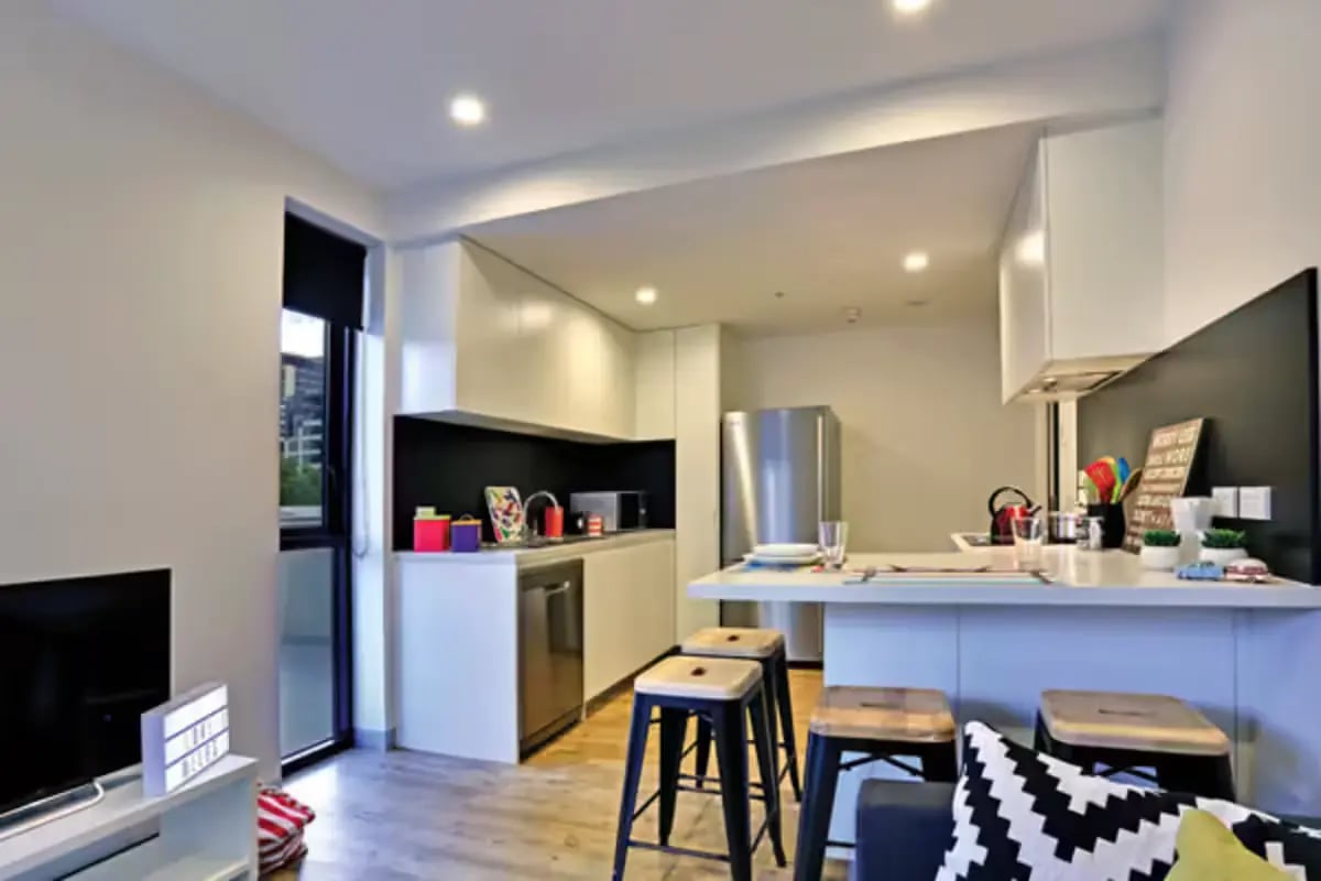 Modern kitchen with stools and TV living area at Scape Melbourne Central in Melbourne Student Accommodation
