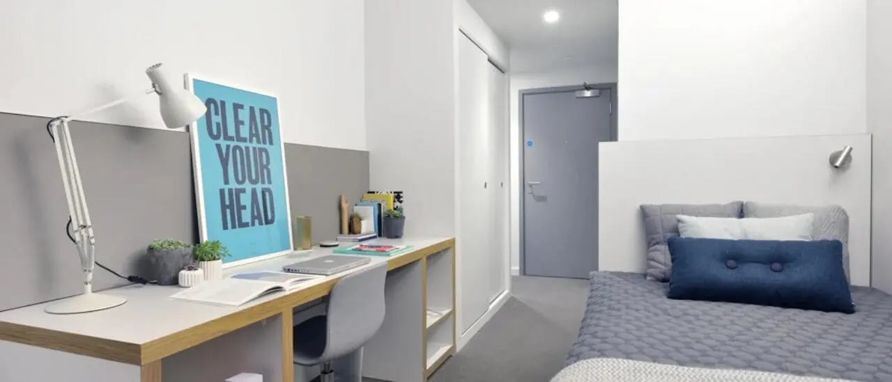 Desk lamp poster bed pillows and door Bedroom at Victoria Hall Kings Cross in London Student Accommodation