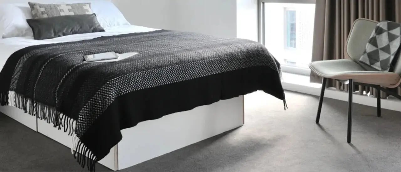 Bed with black throw and pillows modern chair bedroom at Victoria Hall Kings Cross in London Student Accommodation