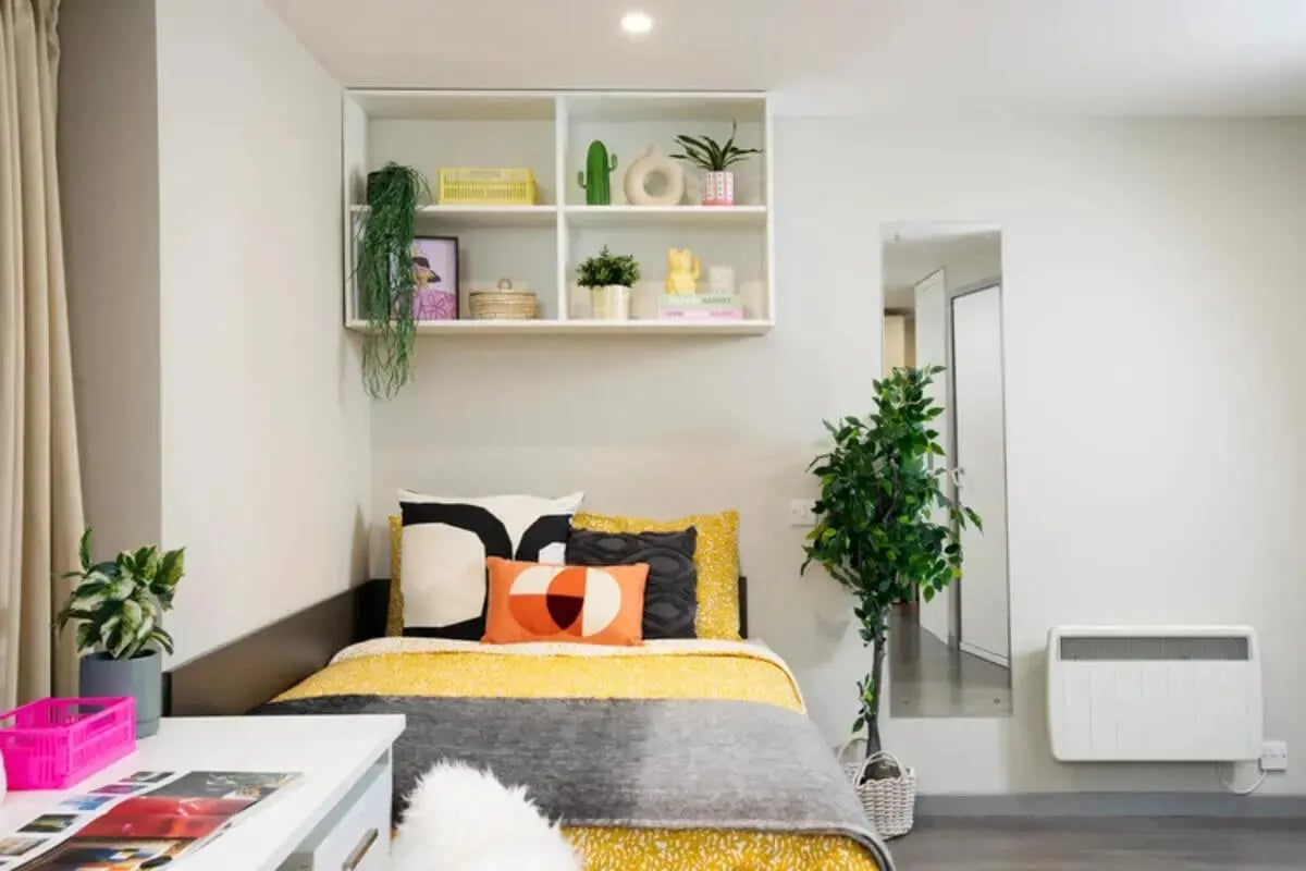 Bed with patterned bedding plants and white shelving Bedroom at Stapleton House in London Student Accommodation
