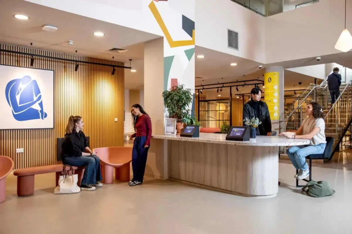 People at reception desk with artwork and seating area. at Stapleton House in London Student Accommodation