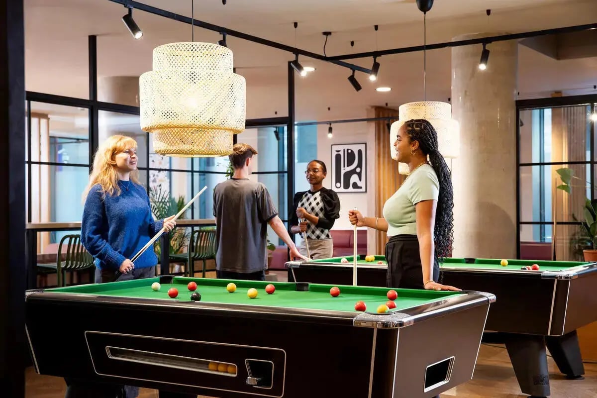 Students play pool with cues on green tables game room at Stapleton House in London Student Accommodation