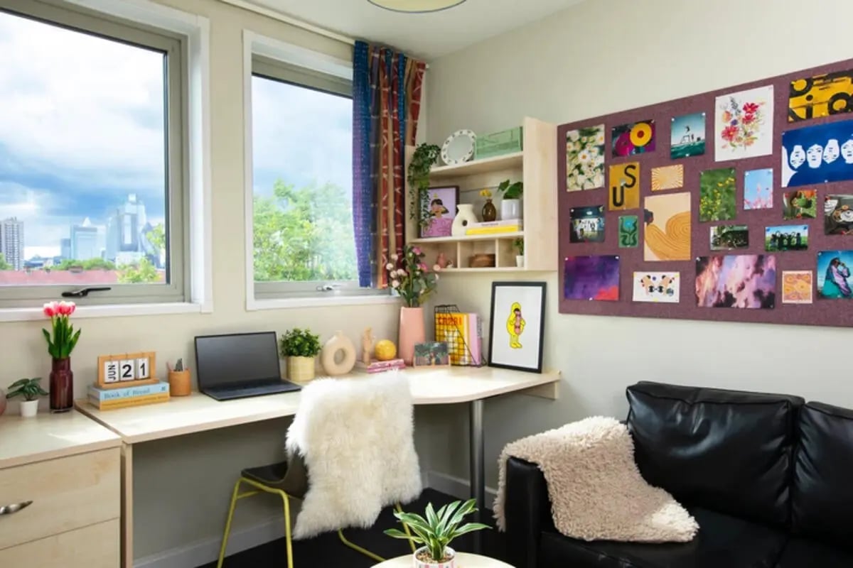 Desk with laptop bulletin board and sofa living room at Quantum Court in London Student Accommodation
