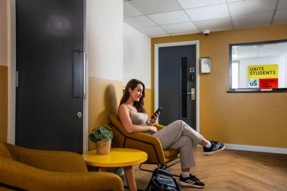 Woman sitting armchair phone yellow table lobby at Quantum Court in London Student Accommodation