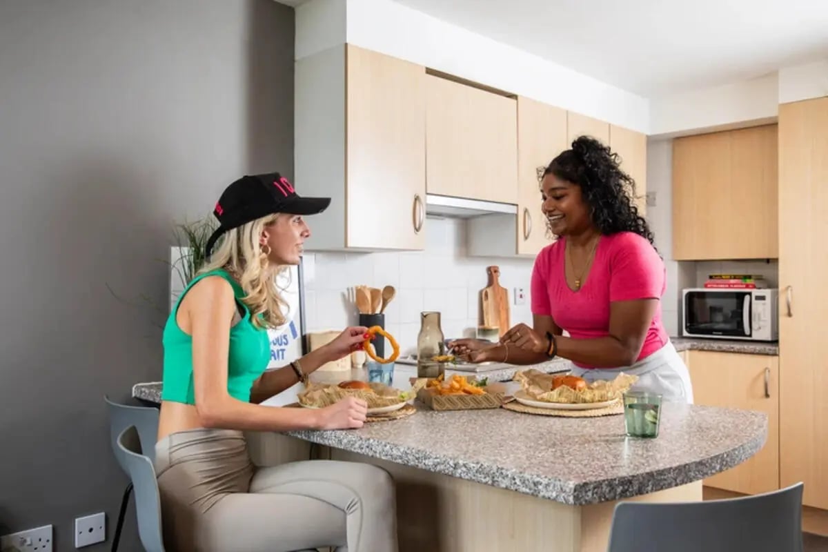 Two women eating food at counter kitchen at Quantum Court in London Student Accommodation