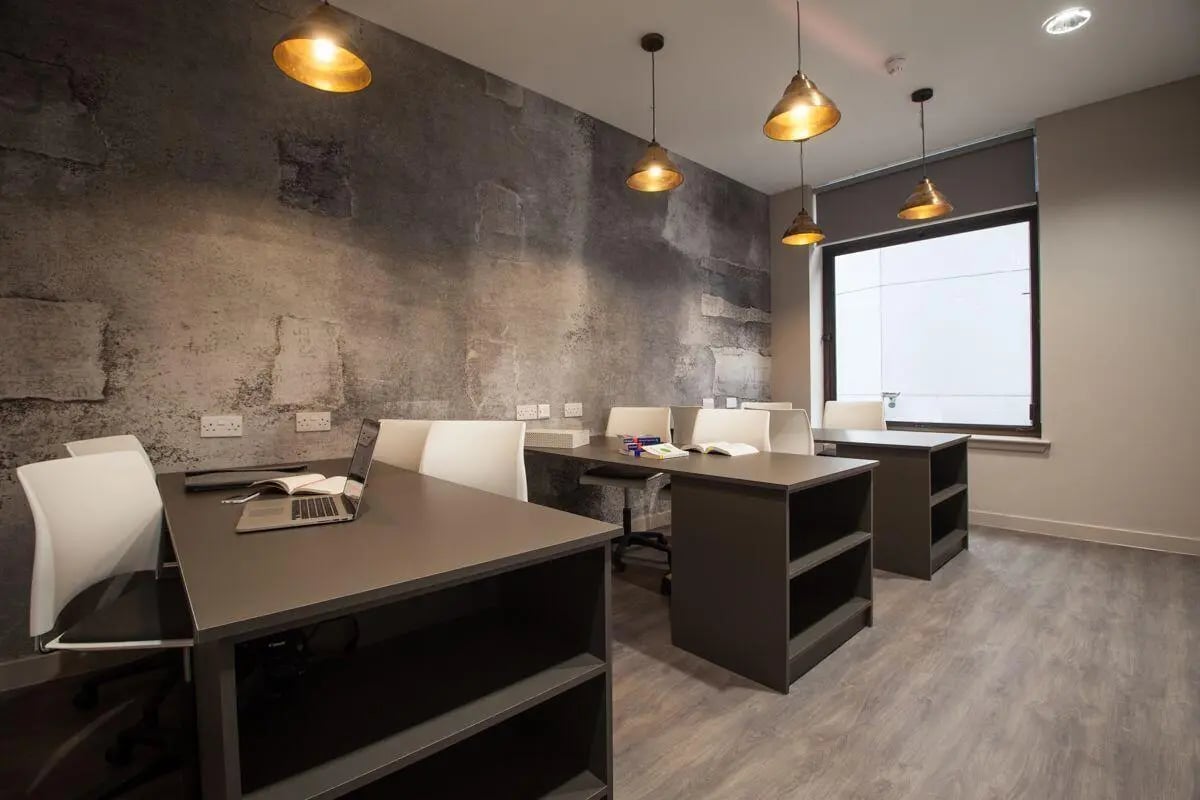 Desks laptops chairs with stone accent wall study area at Bath Street in Glasgow Student Accommodation