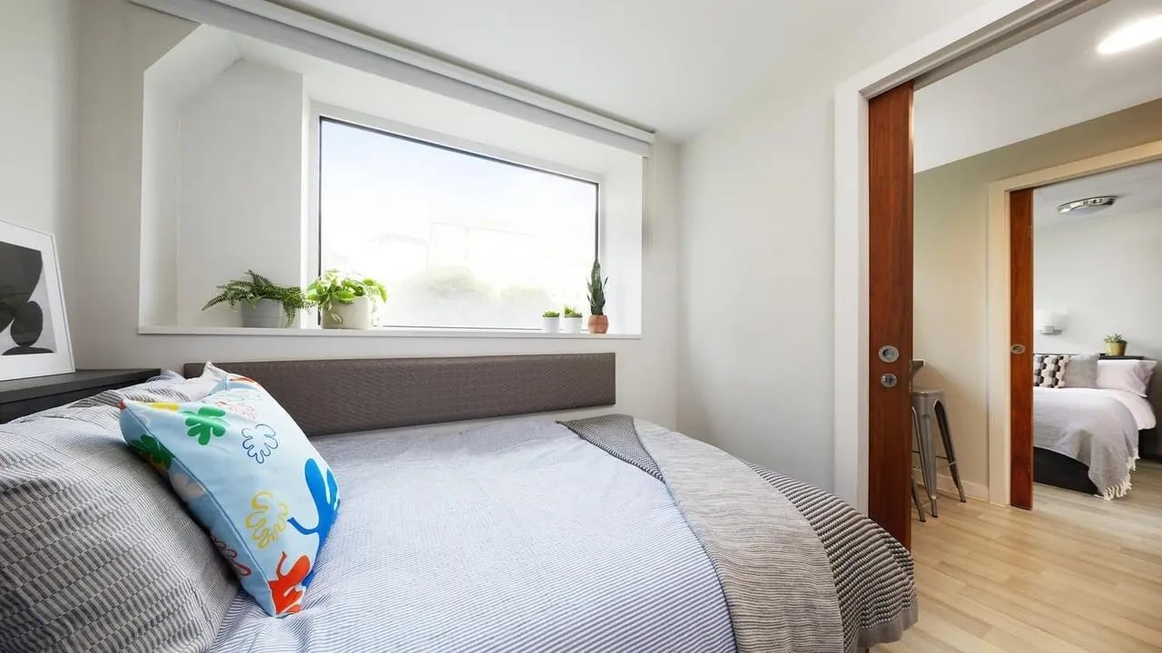 Bed with colorful pillow window plants and door bedroom at Collegiate Tower in Bristol Student Accommodation