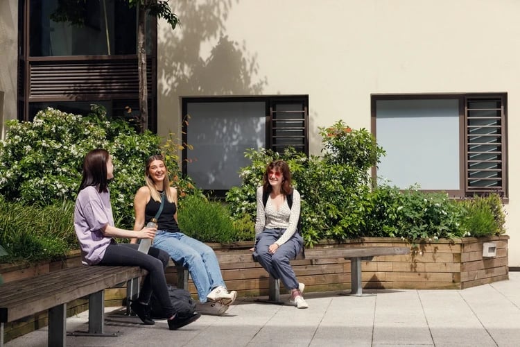 Three students relax on benches exterior at Newgate Court in Newcastle Upon Tyne Student Accommodation