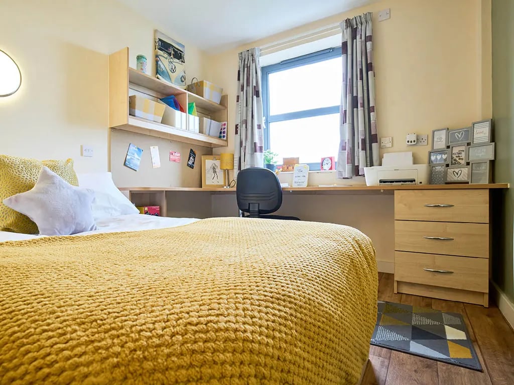 Bed with yellow throw desk with printer and drawers bedroom at Europa in Liverpool Student Accommodation