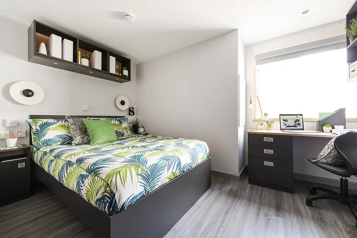 Bed with tropical print linens and desk with laptop bedroom at Yugo Therese House in London Student Accommodation