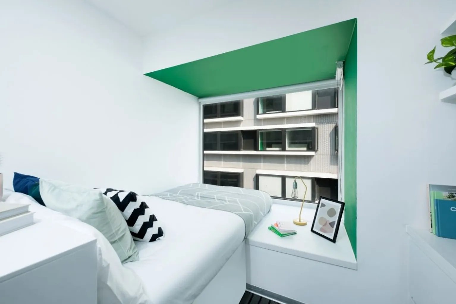 Bed pillows bedside lamp framed picture books bedroom at Scape Mile End in London Student Accommodation