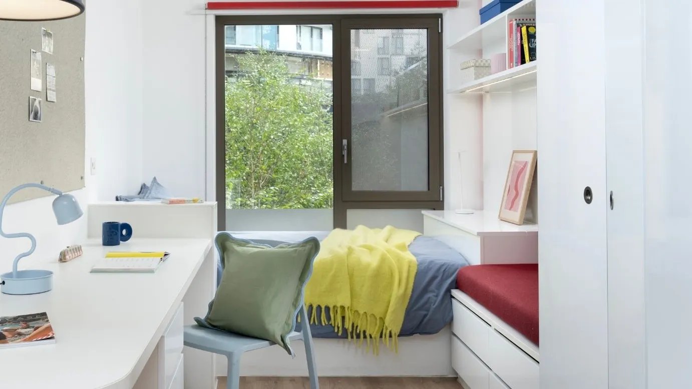 Desk lamp mug chair bed with yellow blanket bedroom at Scape Mile End in London Student Accommodation