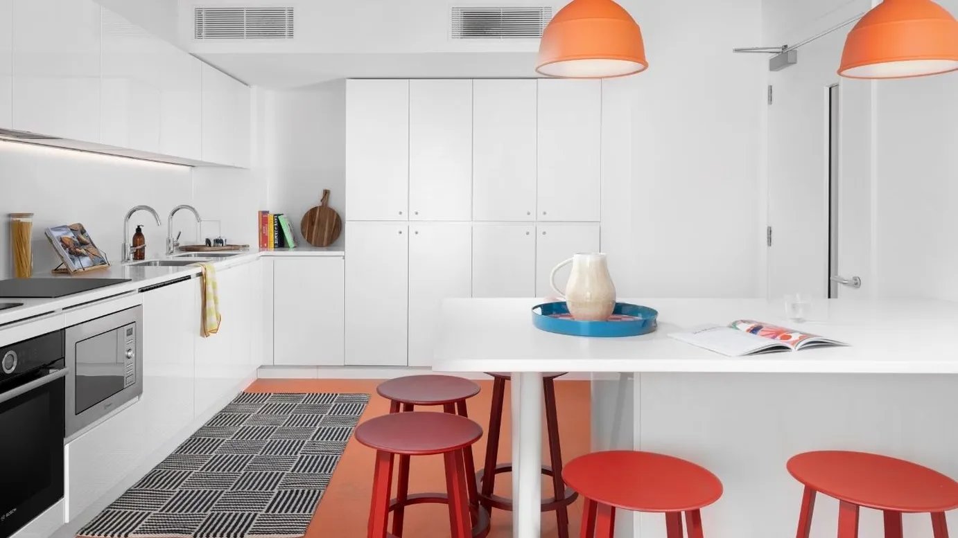 White kitchen with red stools and orange lamps kitchen at Scape Mile End in London Student Accommodation