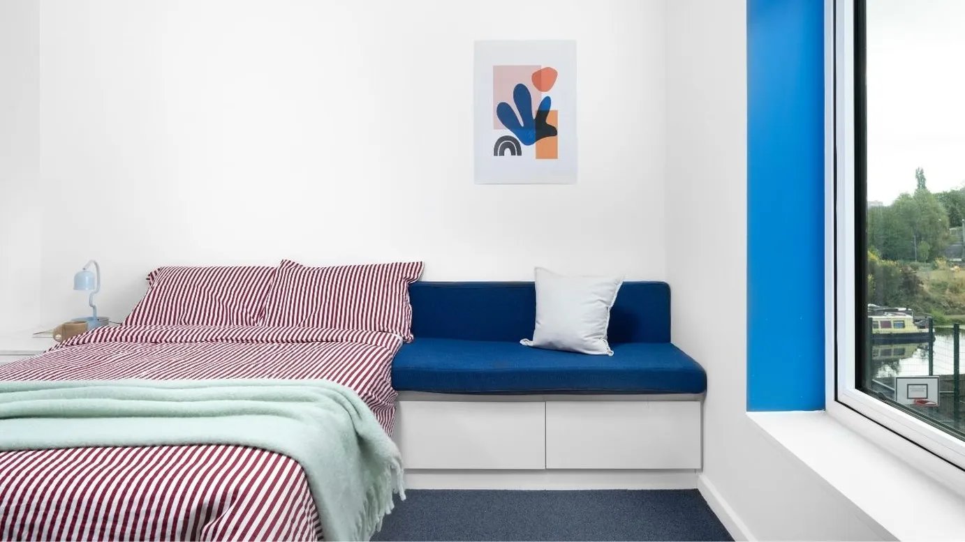 Bed with striped bedding blue bench white pillow bedroom at Scape Mile End in London Student Accommodation