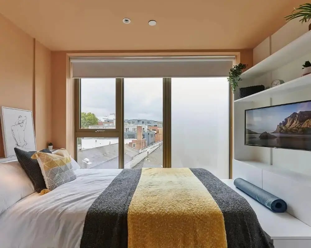 Bed with pillows artwork TV shelves and window bedroom at Host View Studios in London Student Accommodation
