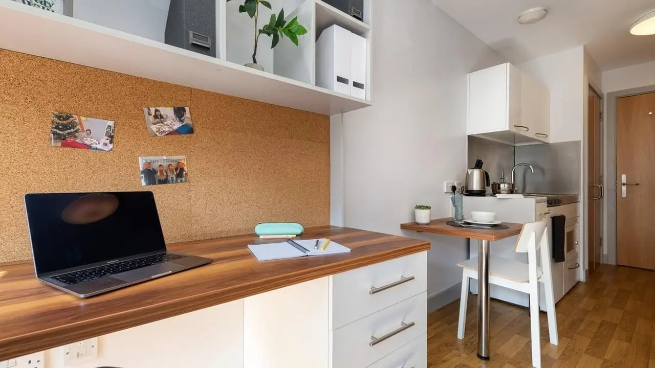 Desk with laptop corkboard and kitchenette studio room at Collegiate Earlsdon Street in Portsmouth Student Accommodation