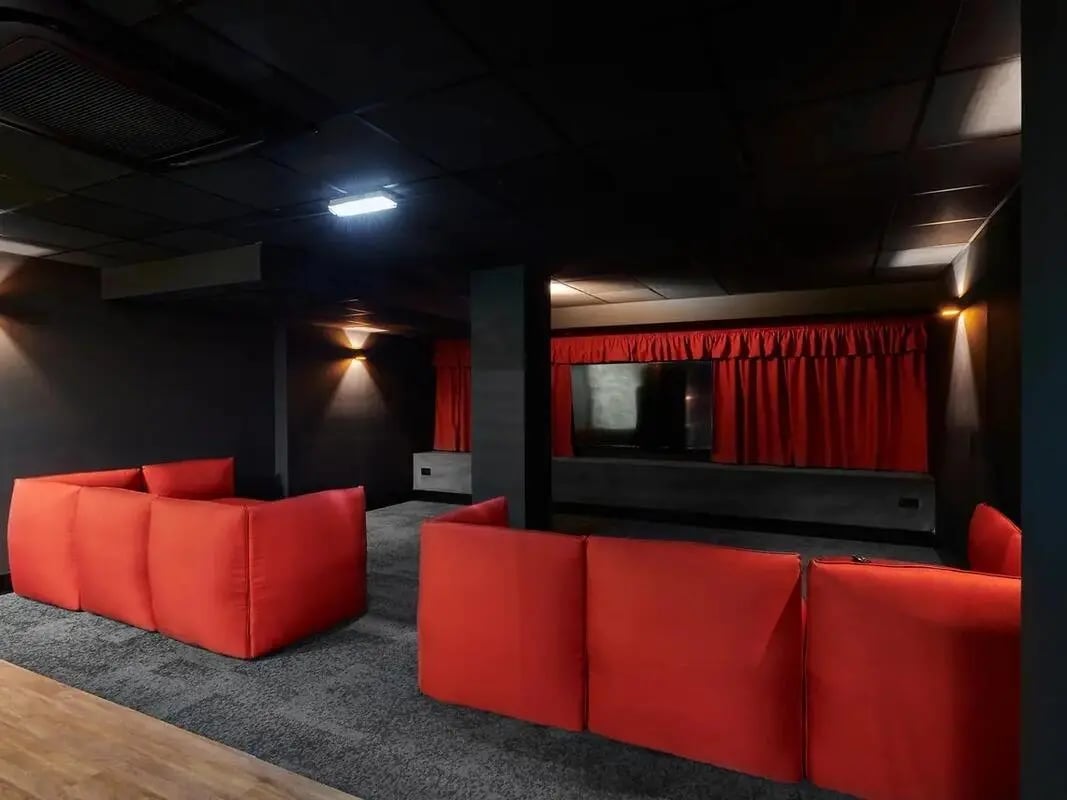 Red sofas facing screen with red curtains cinema room at CB1-Cambridge in Cambridge Student Accommodation