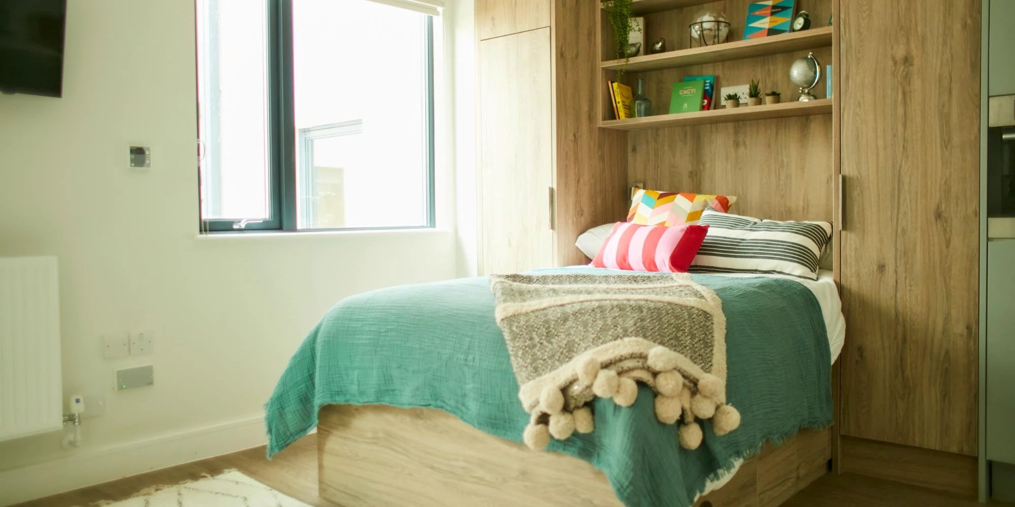 Bed with teal throw and decorative pillows bedroom at Canvas Student - Quintana Gate in Exeter Student Accommodation