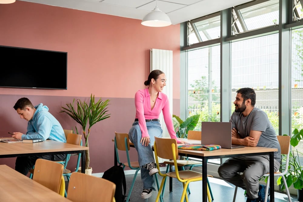 Students at tables with laptop and plants communal area at Moonraker Point in London Student Accommodation