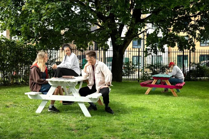 People sitting on picnic tables outdoors green space exterior at Adam Street Gardens in Cardiff Student Accommodation