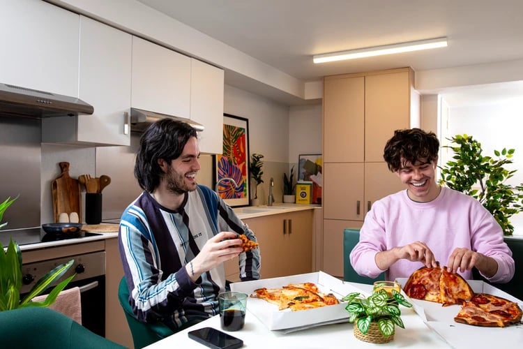 Two students eating pizza in a kitchen at Station Court in London Student Accommodation