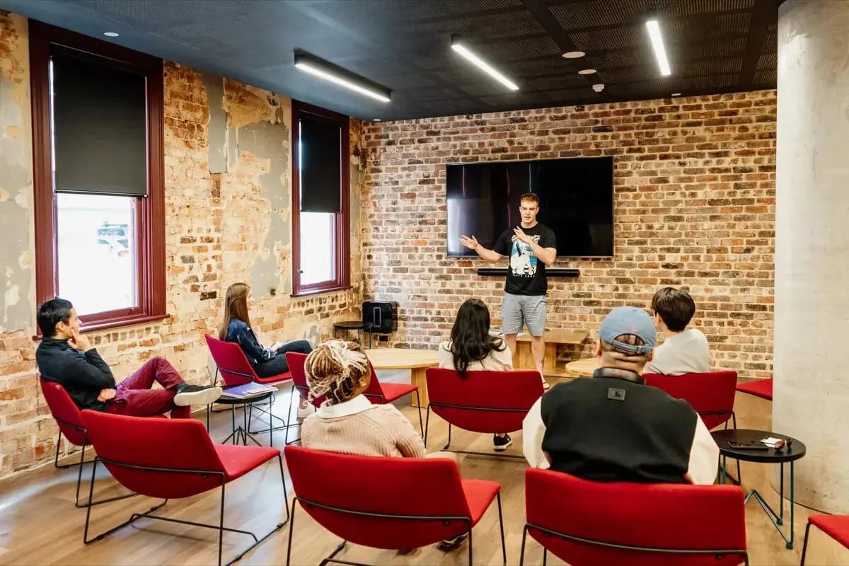 People sitting on red chairs watching speaker living room at Perth Central in Perth Student Accommodation