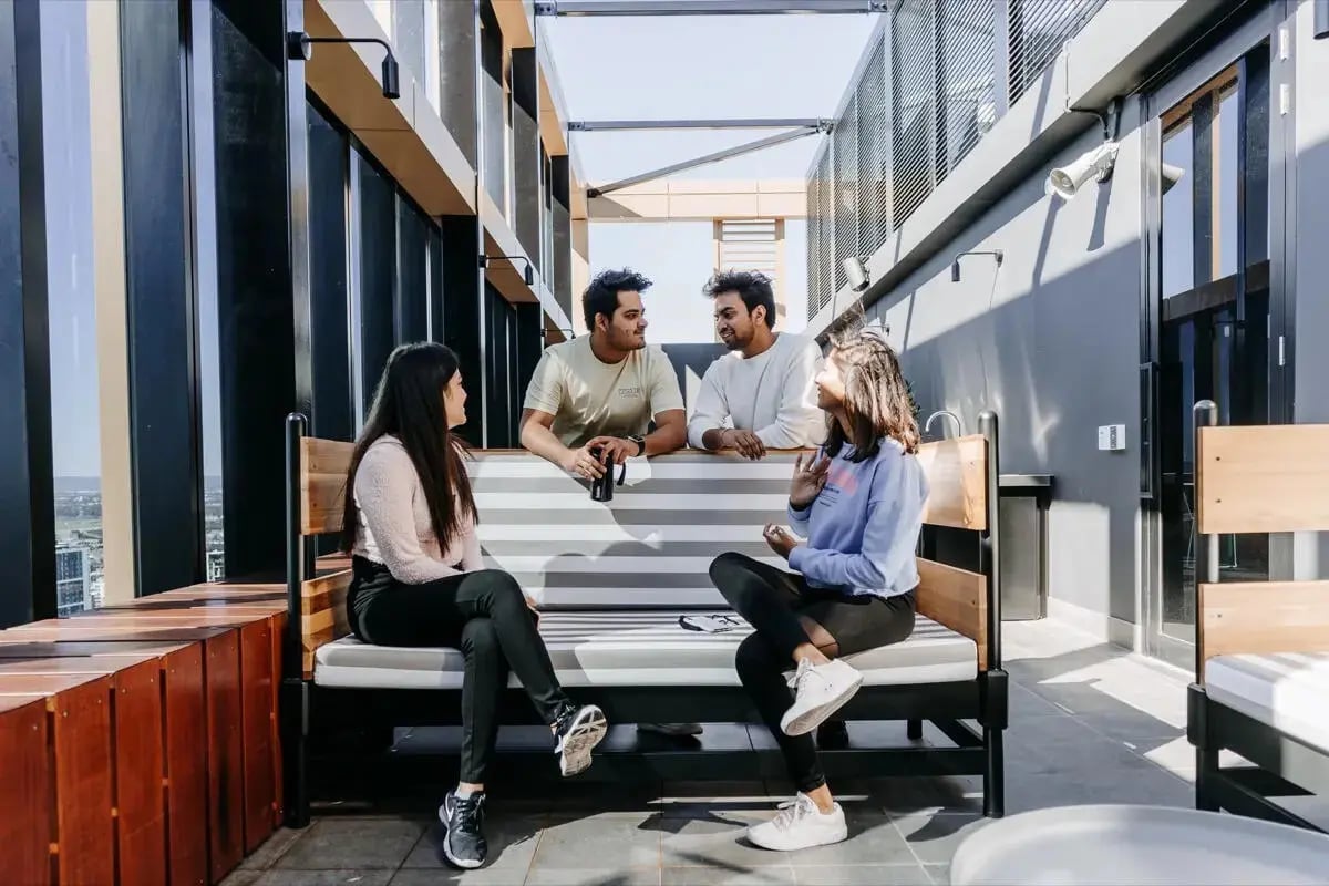 Four students chatting on a striped bench outdoor living room at Perth Central in Perth Student Accommodation