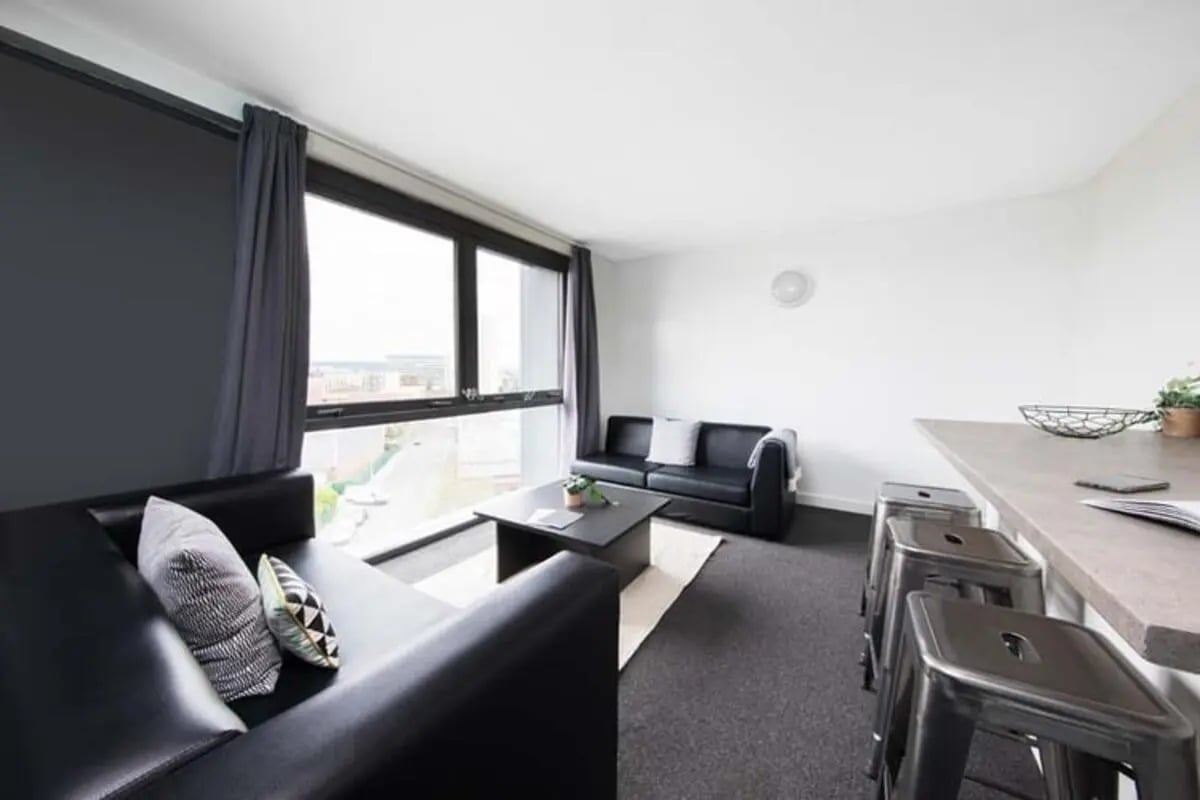 Black sofas coffee table stools kitchen area living room at Kyle Park House in Glasgow Student Accommodation