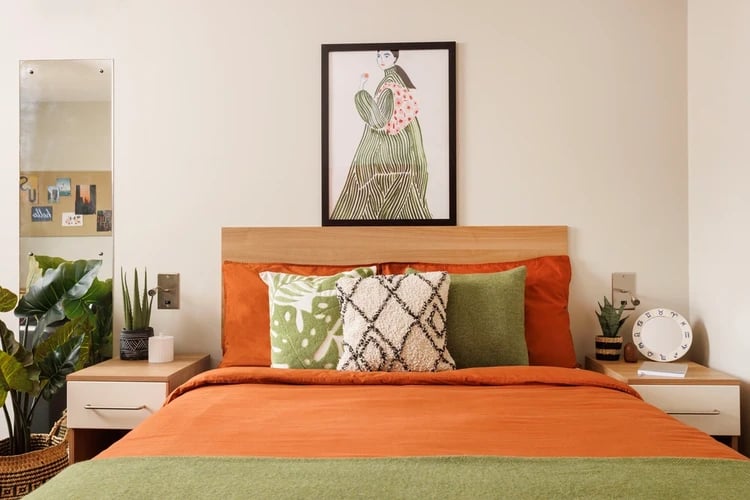 Bed with orange bedding green pillows artwork mirror bedroom at Chalmers Street in Edinburgh Student Accommodation