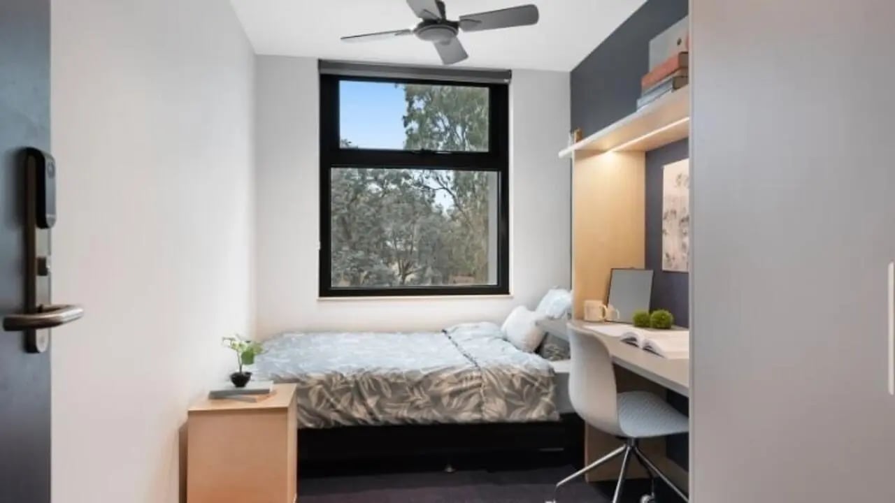 Bed bedside table ceiling fan desk chair bedroom at La Trobe University - North and South Apartments in Melbourne Student Accommodation
