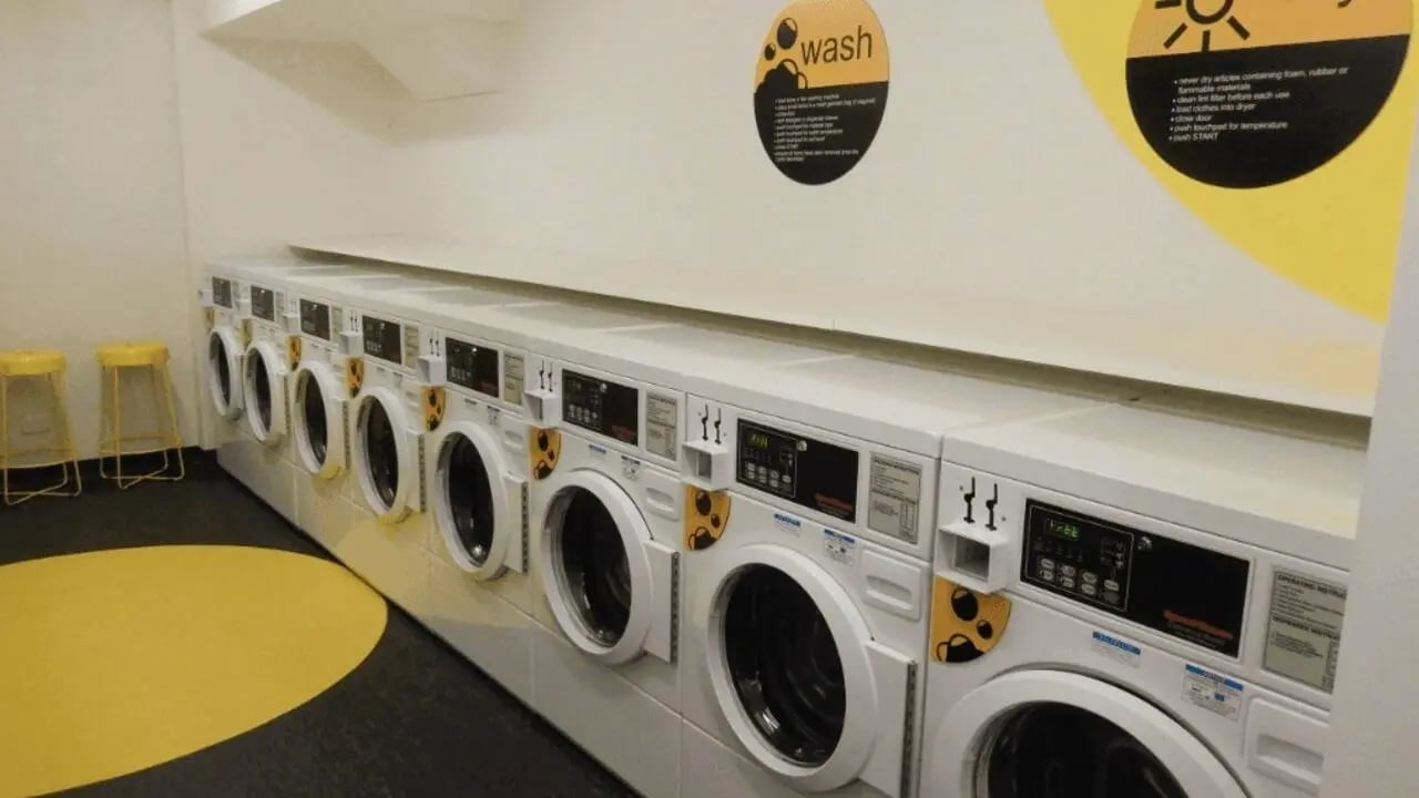 Multiple washing machines and yellow stools laundry room at La Trobe University - Menzies College in Melbourne Student Accommodation