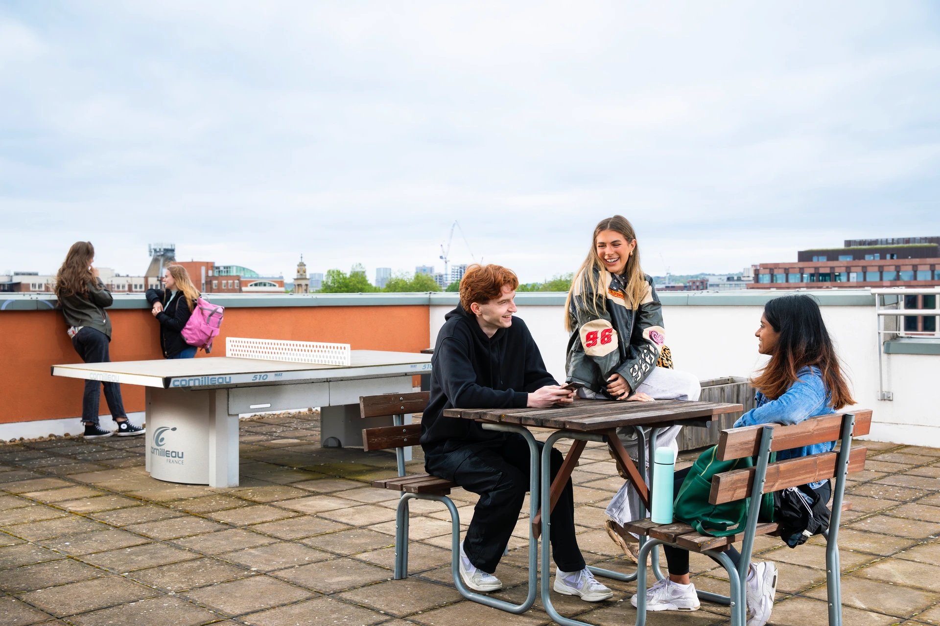 Students socialize at table near ping pong table outdoor area at Beaumont Court in London Student Accommodation