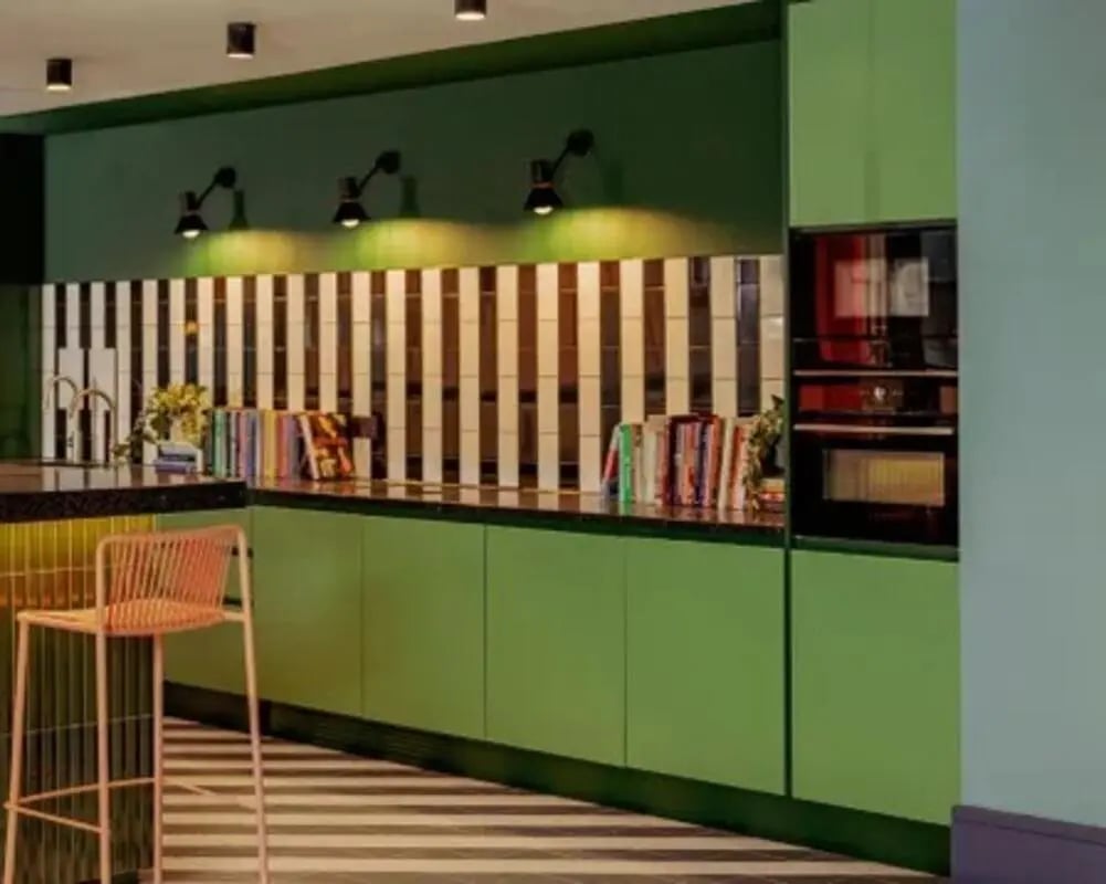 Green cabinets pink stool books oven kitchen at Scape Hammersmith in London Student Accommodation