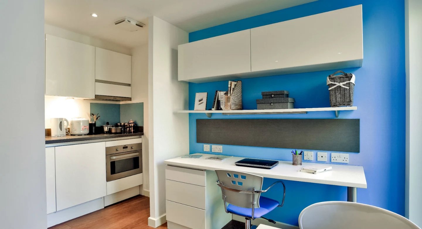 White cabinets desk chair and kitchen area study room at Griffon Studios in London Student Accommodation
