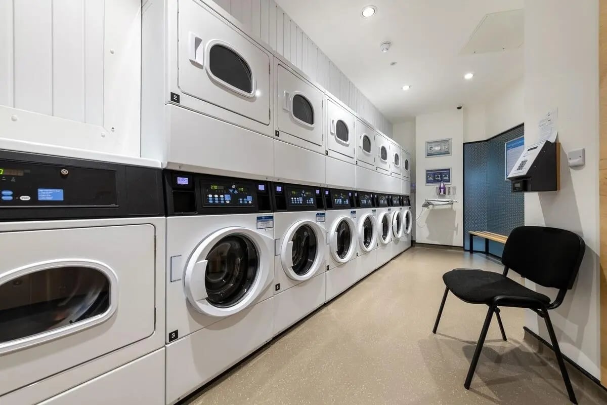 Stacking washers and dryers with control panels and chairs laundry room at Collegiate Park House in Southampton Student Accommodation