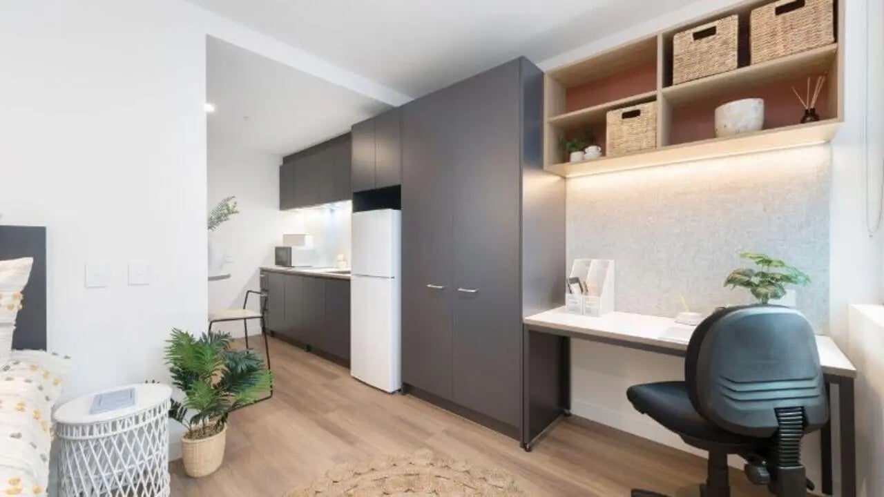 Desk, chair, shelves, and kitchen setup living room. at UniLodge Melbourne Flagstaff in Melbourne Student Accommodation