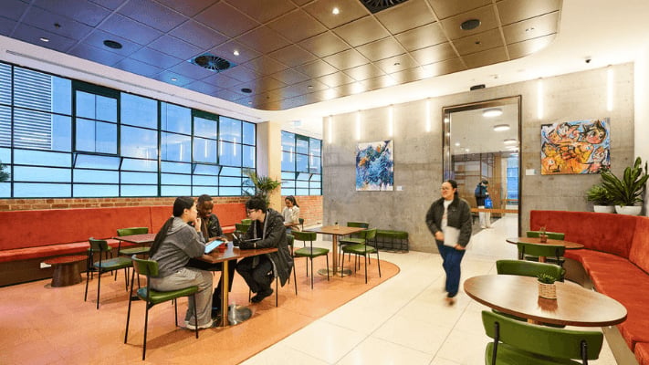 Students at tables with orange benches and modern art living room at UniLodge Melbourne Flagstaff in Melbourne Student Accommodation