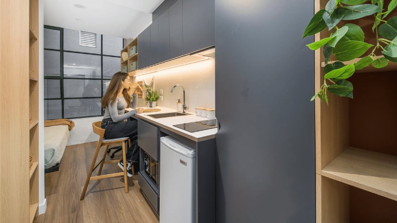 Woman at kitchenette counter next to bed Studio apartment at UniLodge Melbourne Flagstaff in Melbourne Student Accommodation